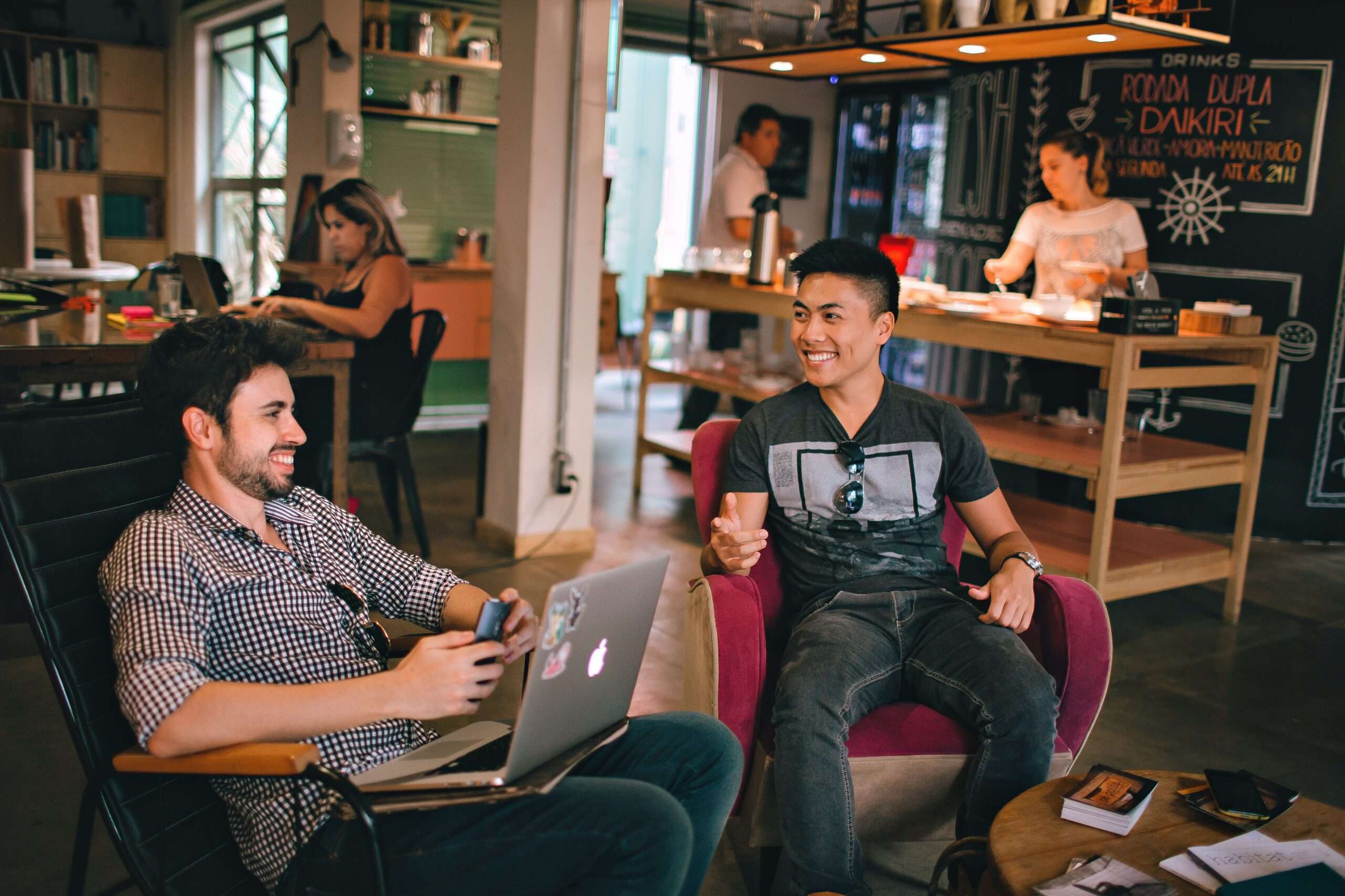 Photo of two friends working and laughing together at a coffee shop.
